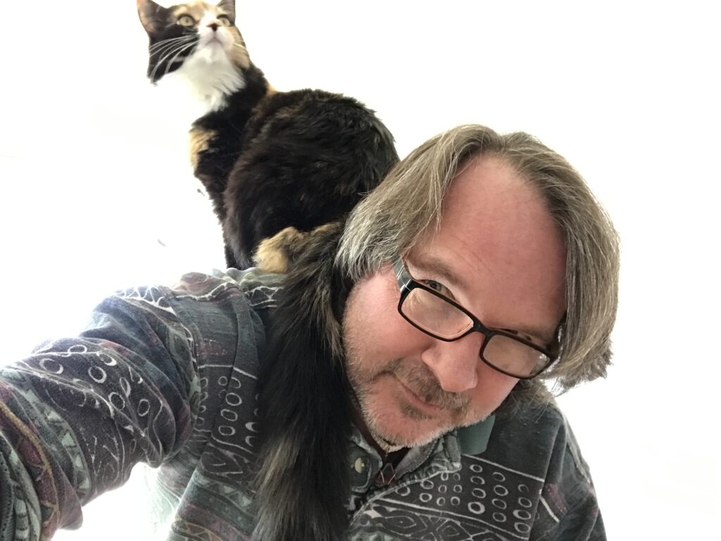 A person crouched over with a long-haired calico cat sitting on their back.